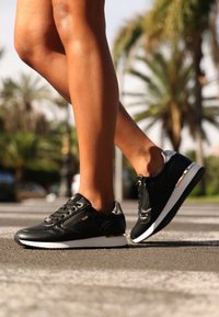 Svarta syntetiska sneakers med snörning fram, metalliska accenter, en texturerad sula och en snygg design. Passar för avslappnad användning.