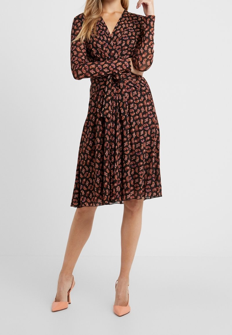 Svart omlottklänning med långa ärmar, prydd med ett färgglatt djurtryck, med cinchad midja och en utställd kjol, tillsammans med ljusrosa klackar.