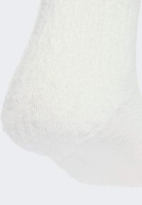 White fuzzy sock made of soft knit material, featuring a textured surface and rounded toe, with a slight stretch at the opening.