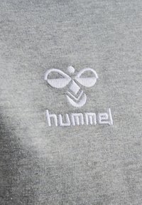 Tessuto di cotone grigio con un logo ricamato bianco raffigurante un'ape e la parola "hummel" sotto di essa.