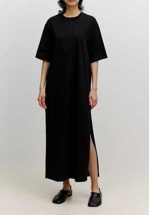 Black, ankle-length dress with short sleeves, round neck, and side slits. Made of soft fabric, featuring a relaxed fit. Paired with black flat shoes.