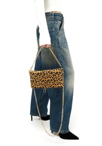 Borsa a mano con stampa leopardata e tracolla in catena dorata, forma rettangolare, materiale in tessuto e chiusura con zip. Indossata con jeans larghi e tacchi.