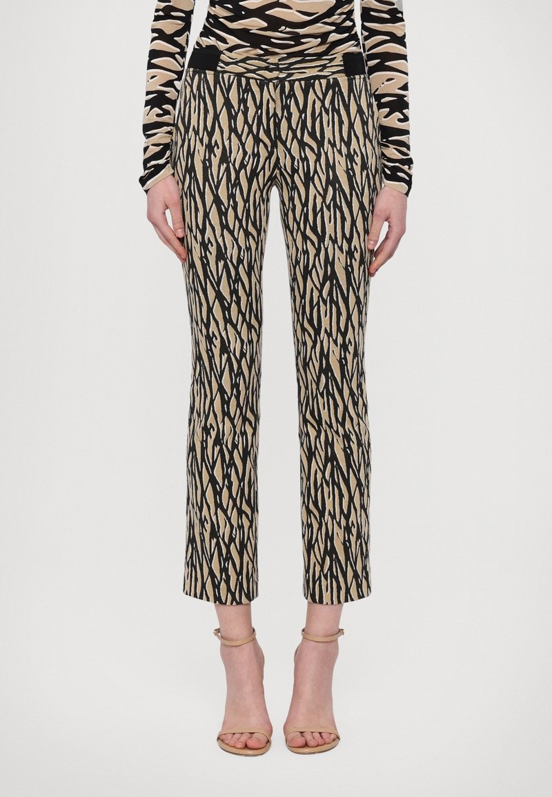 Pantalon slim à motif abstrait beige et noir porté avec un haut assorti à motif et des talons à bride cheville beige.