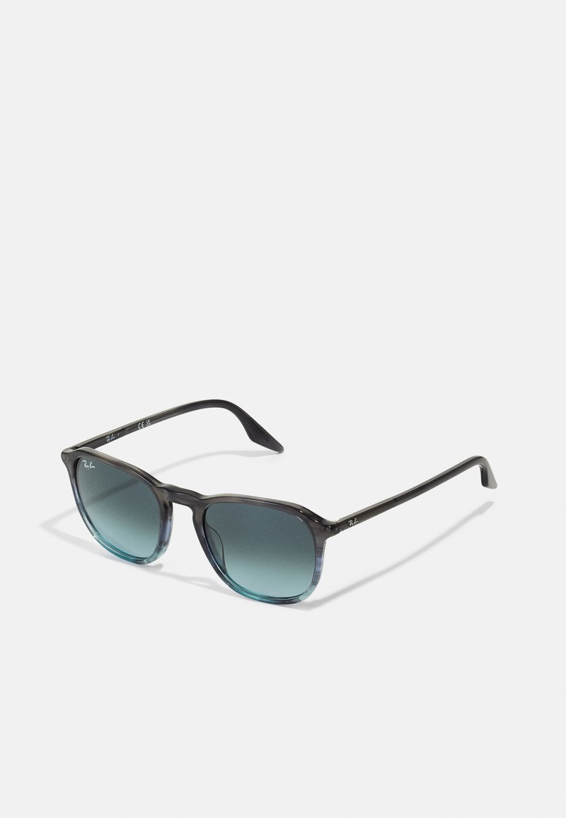 Ochelari de soare cu ramă pătrată din plastic translucid de culoare gri închis. Lentilele în degrade de culoare teal și brațele subțiri de culoare neagră au o marcaj subtil.