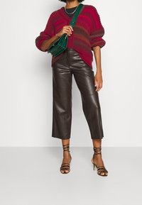 Kraftig röd stickad tröja med v-ringning, bruna fusk läder korta byxor och svarta högklackade sandaler med remmar. Grön axelremsväska.