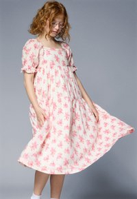 Light pink cotton dress with floral pattern, square neckline, puffed sleeves, and gathered waist, reaching below the knee.