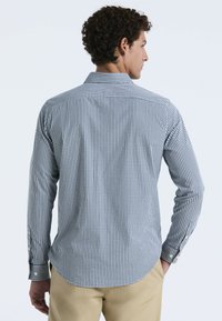 Herenoverhemd met lange mouwen in een marineblauw en wit geruit patroon, van katoen materiaal, met knopenmanchetten, een afgeronde onderkant en een rugpasdetail.