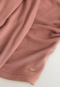 Ribbade tyger i dammig rosafärg, med en guldtonad märketikett. Mjuk textur med subtil stretch, perfekt för avslappnad klädsel.