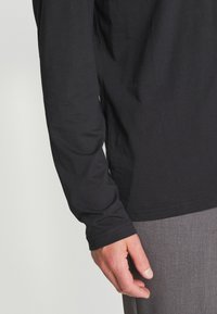 Langärmliges schwarzes Shirt aus Baumwolle mit glatter Textur, körpernaher Passform und schlichtem Design. Der Saum ist gerade und ohne sichtbare Verzierungen.