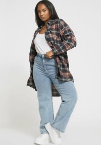 Flanellen overhemd in marineblauw, rood en wit ruitpatroon met lange mouwen, gecombineerd met high-waisted lichtblauwe jeans en witte sneakers.