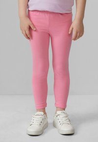 Hellrosa Leggings aus dehnbarem Material, figurnahes Design, elastischer Bund, kombiniert mit weißen Sneakern mit strukturierter Oberfläche.