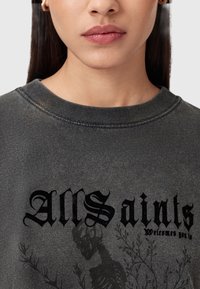Felpa grigia scura con scollo a rotonda, caratterizzata da una stampa testurizzata con la scritta "All Saints" e un design di scheletro con accenti floreali.