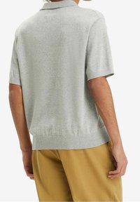 Grå kortärmad pullover med ribbad krage och fåll. Mjuk, slät struktur. Bärs med ljusbruna byxor.