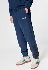 Marinblå sportbyxor med elastisk midja och fickor, med svarta sidodetaljer och en vit logotyp på låret.