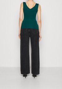 Tealfärgad ärmlös topp med V-ringning och rynkning vid axlarna, kombinerad med vida svarta jeans, detaljerad med bakfickor och rå kant.