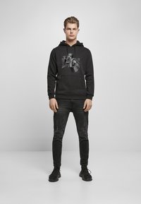 Zwarte hoodie met een afbeelding van een persoon op de voorkant, gedragen met zwarte jeans en zwarte sneakers. Casual pasvorm, van katoen.