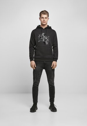 Black hoodie featuring a graphic of a person on the front, worn with black jeans and black sneakers. Casual fit, cotton material.