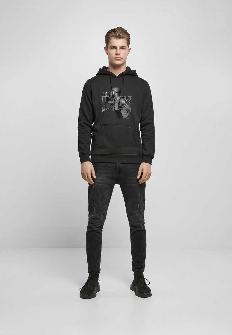 Zwarte hoodie met een afbeelding van een persoon op de voorkant, gedragen met zwarte jeans en zwarte sneakers. Casual pasvorm, van katoen.