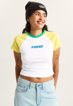 Hvid crop-top t-shirt med grønne og gule raglanærmer, med en blå "Vans"-logo foran. Kombineret med lyseblå denimshorts.