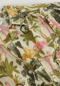 Chemise à manches courtes avec imprimé d'animaux tropicaux et de palmiers en vert, rose, orange et noir sur tissu beige.