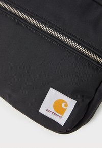 Zaino in tessuto nero con una vistosa cerniera argento e un'etichetta bianca con un logo giallo e testo. Materiale resistente con una finitura texture.