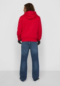 Felpa rossa con cappuccio, dal taglio comodo e polsini a coste. Abbinata a jeans in denim blu con gamba dritta e tasche posteriori.