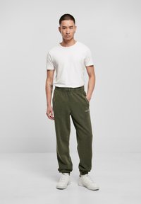 Olivengrønne sweatpants med elastisk talje, sidelommer og ribbede manchetter, parret med en almindelig hvid t-shirt og hvide sneakers.