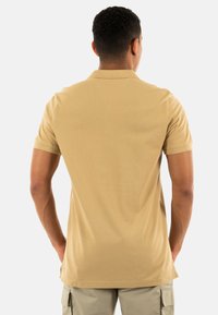 Polo de color beige con una textura suave, mangas cortas y un collar clásico. Presenta un corte ajustado y un sutil detalle en la costura trasera.