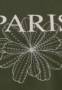 Donkergroene katoenstof met een groot wit omrand bloemontwerp met stippellijnen. Het woord "PARIS" is boven de bloem gedrukt.