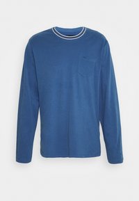 Langærmet blå T-shirt lavet af blødt stof. Har en rund hals med hvide striber og en brystlomme med et diskret logo.