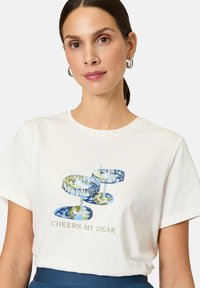 White cotton t-shirt featuring a graphic design of two cocktails with blue and green accents, and the text "CHEERS MY DEAR" in gold.