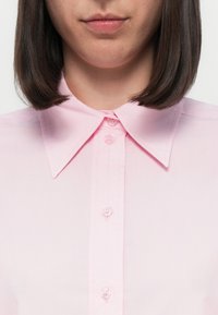 Lys rosa skjorte med klassisk krage og syv knapper foran, laget av et glatt stoff med en subtil glans.