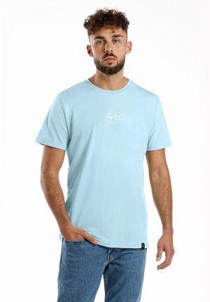 Helles blaues Baumwoll-T-Shirt mit kurzen Ärmeln, Rundhals und einem weißen Grafiklogo auf der Brust. Getragen mit blauen Jeans.
