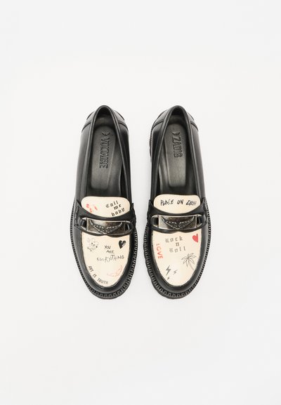 Black leather loafers featuring a decorative strap, with cream insoles displaying varied handwritten graphics and symbols. Low-profile design.