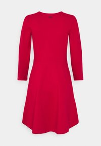 Czerwona sukienka z długim rękawem, wykonana z elastycznego materiału, z dopasowaną górą, rozkloszowanym dołem i okrągłym dekoltem. Przedstawiony widok z tyłu.