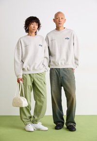 Gray sweatshirts with colorful logo; green cargo pants; light sneakers and black shoes; white handbag; minimalistic design, casual fit.