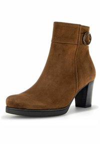Bottine en daim marron avec un bout arrondi, un talon noir de hauteur moyenne et un accent circulaire décoratif sur la bride de la cheville.