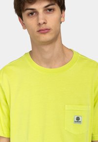 Light yellow T-shirt made of cotton with a crew neckline, short sleeves, and a patch pocket featuring a branded label.