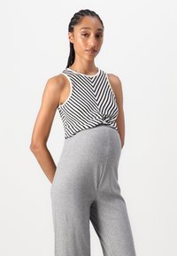 Gestreift schwarz-weißes Tanktop mit verdrehter Vorderseite, kombiniert mit hellgrauen, gerippten weiten Hosen. Glatte Textur, lässige Passform.
