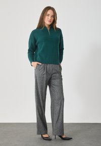 Τελαμίνης πλεκτός πούλος σε τιρκουάζ απόχρωση με μισό φερμουάρ, συνδυασμένος με γκρι παντελόνι σε φαρδιά γραμμή. Μαύρες γόβες με μυτερή μύτη ολοκληρώνουν το σύνολο.