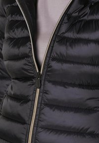 Sort polstret vest med vandrette, quiltede sektioner, en glat stof tekstur og en sølvfarvet lynlås foran.