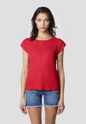 Rdeča majica s kratkimi rokavi iz mehkega materiala s subtilnimi bleščečimi poudarki, združena z jeans kratkimi hlačami. Pasaža je ohlapna in priložnostna.