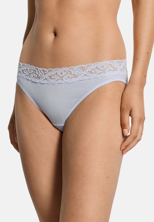 Vrouw draagt lichtblauwe bikini-stijl ondergoed met kanten rand, toont de buik en bovenbenen tegen een witte achtergrond.