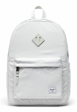 Sac à dos Herschel blanc avec poche avant zippée et écusson en cuir en forme de losange sur un fond uni.