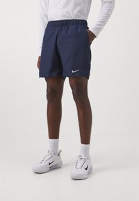 Tamsiai mėlynos Nike šortai su elastine liemene, šoninėmis kišenėmis ir baltu logotipo akcentu. Pagaminti iš glotnaus audinio, tinkami aktyviam sportui.