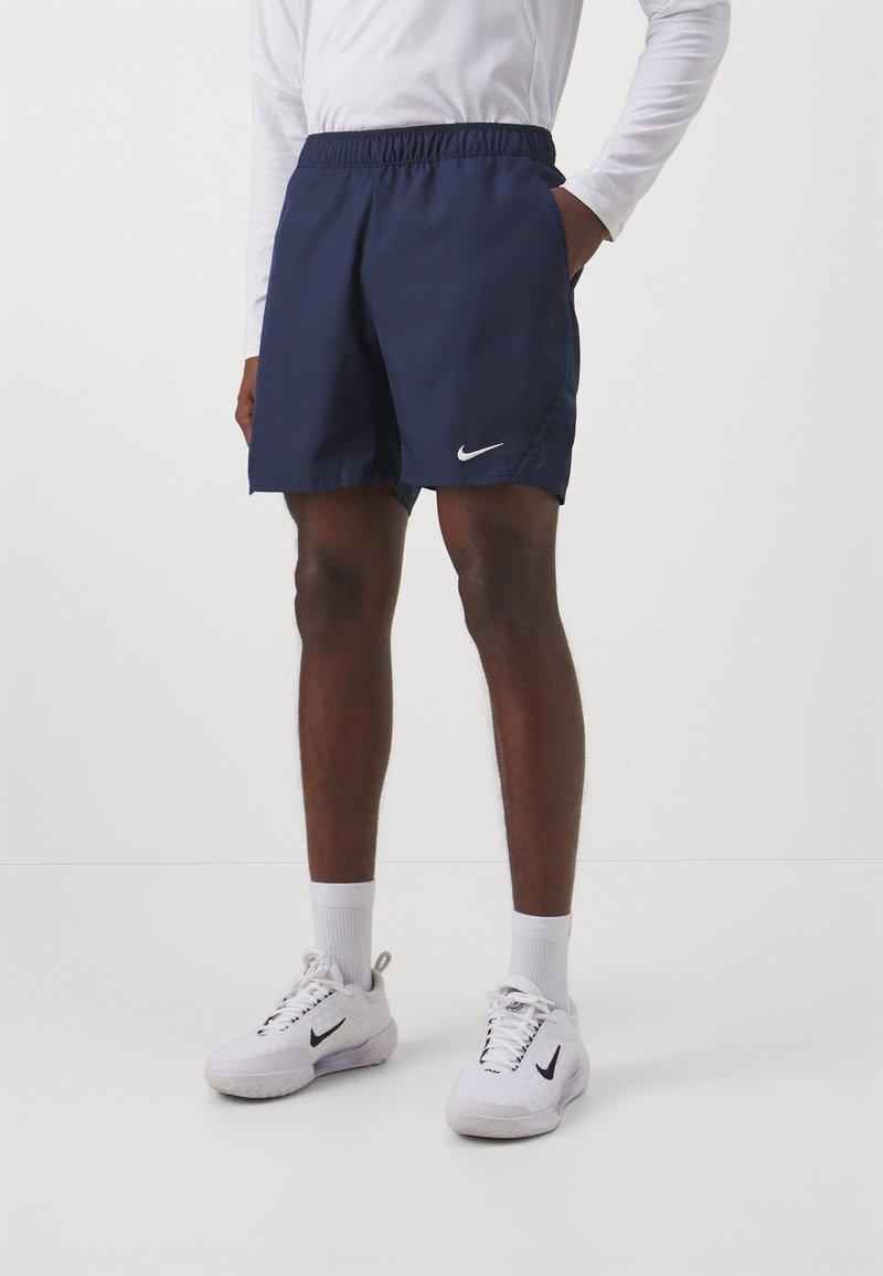 Tamsiai mėlynos Nike šortai su elastine liemene, šoninėmis kišenėmis ir baltu logotipo akcentu. Pagaminti iš glotnaus audinio, tinkami aktyviam sportui.