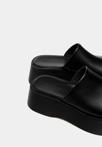Mule neri con piattaforma realizzati in pelle liscia. Presentano una tomaia ampia e un tacco spesso e chunky. Design semplice senza hardware o motivi visibili.