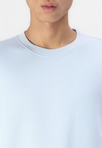 Light blue sweatshirt with a ribbed neckline, featuring a smooth texture and a classic crew cut design. Close-up view from the chest upward.