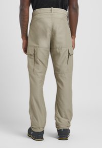 Beige Cargo-Hosen mit lockerer Passform, ausgestattet mit zwei Seitentaschen und einem hohen Bund, aus leichtem Stoff. Kombiniert mit dunklen Schuhen.