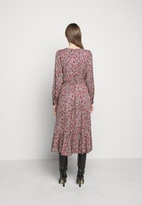Długa, midi sukienka z długim rękawem w czerwono-niebiesko-białym wzorze paisley. Rozkloszowany dół, dopasowana talia, miękka tkanina i okrągły dekolt.